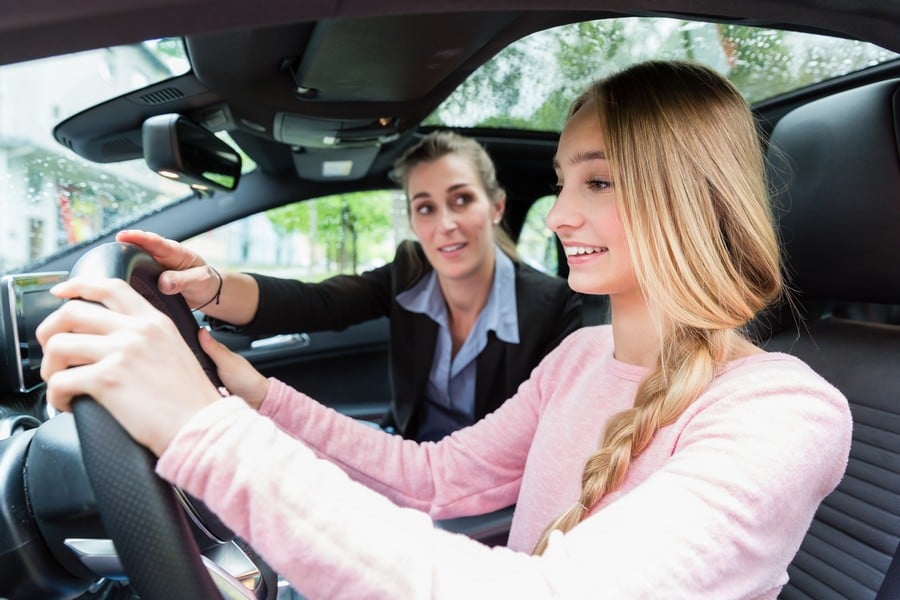 Student on wheel of car in driving lesson with her teacher learning to drive